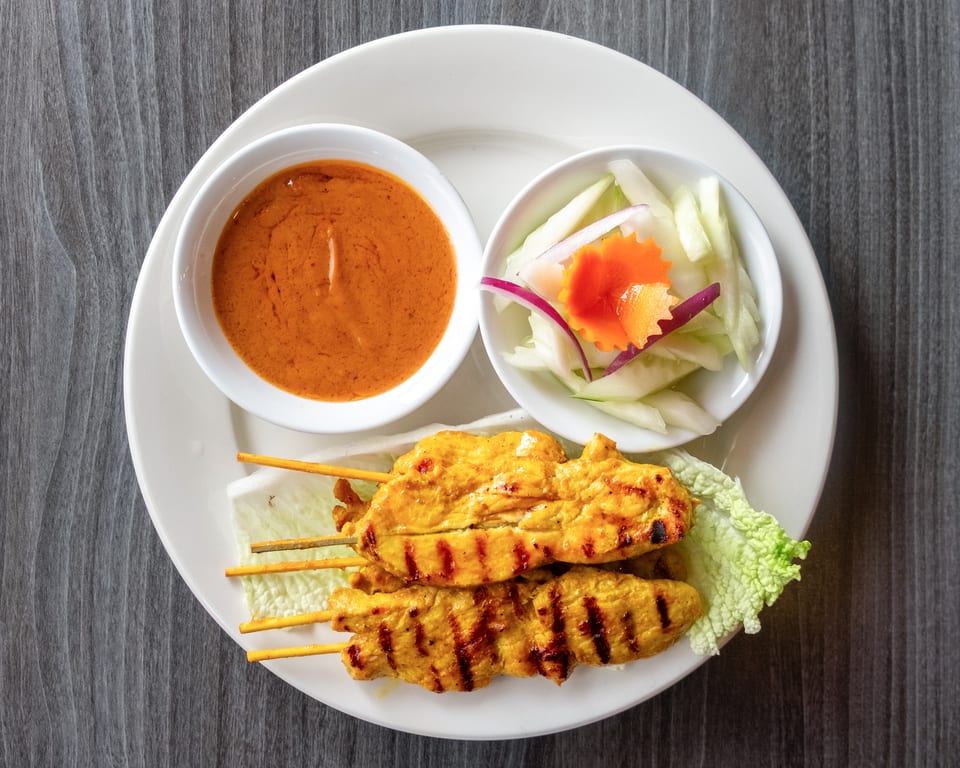 Grilled chicken satay skewers with peanut sauce and a side of cucumber salad.