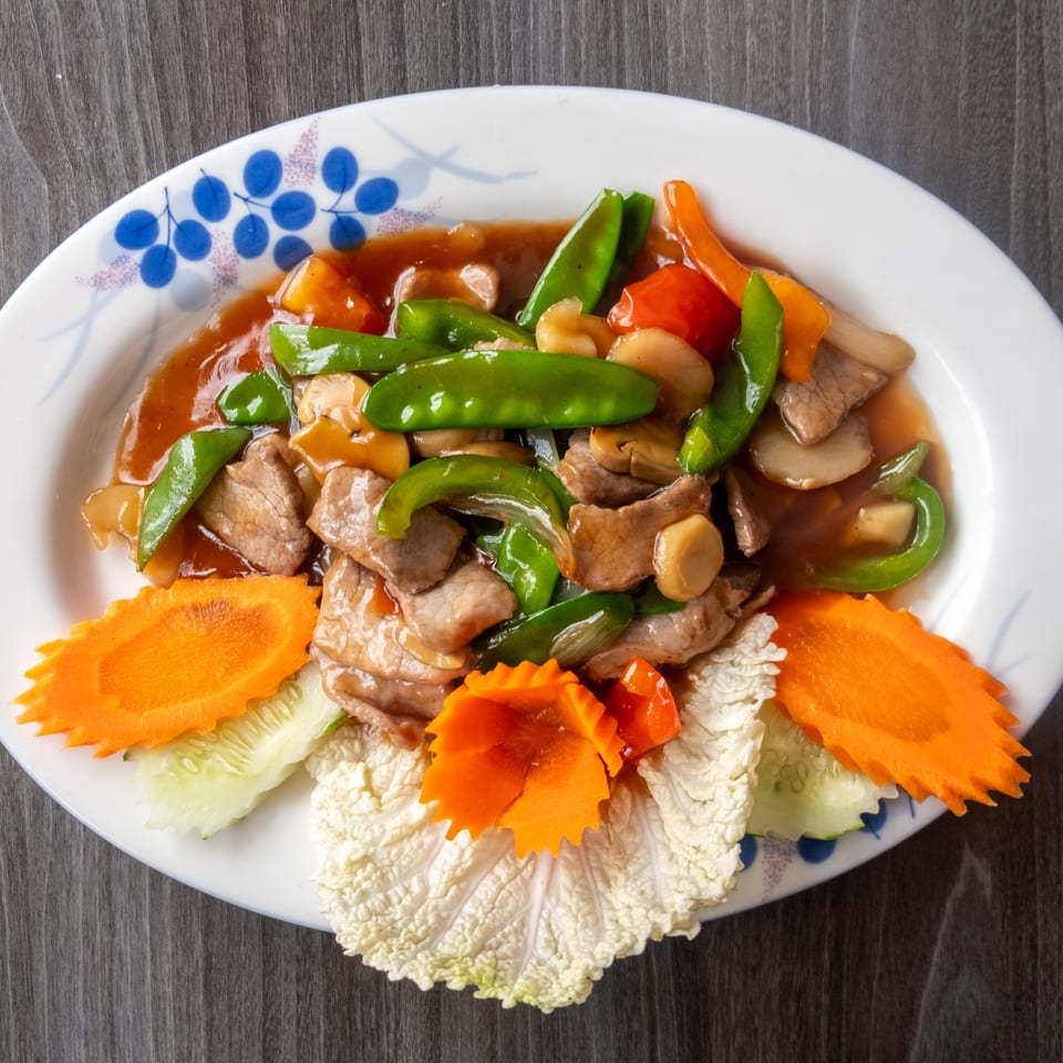 Savory beef stir-fry with vibrant green peppers, mushrooms, and carrots on a white plate.