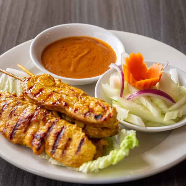 Grilled chicken satay skewers with peanut sauce and a side of cucumber salad.