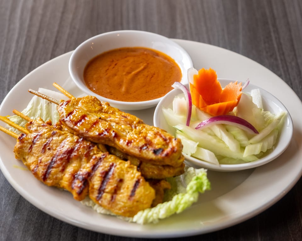 Grilled chicken satay skewers with peanut sauce and a side of cucumber salad.