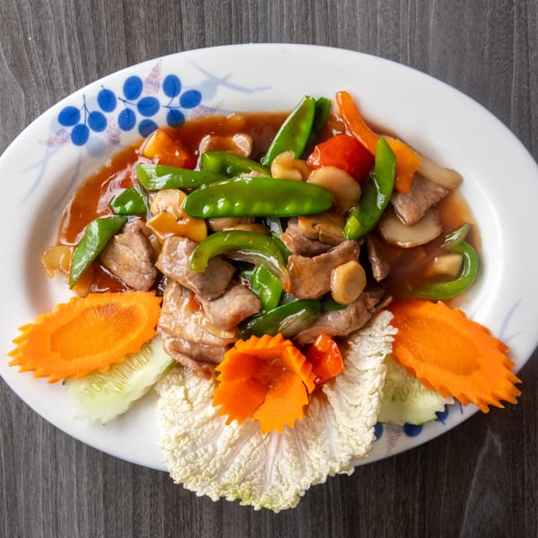 Slices of beef with green peppers, mushrooms, and carrots in a brown sauce on a white plate.