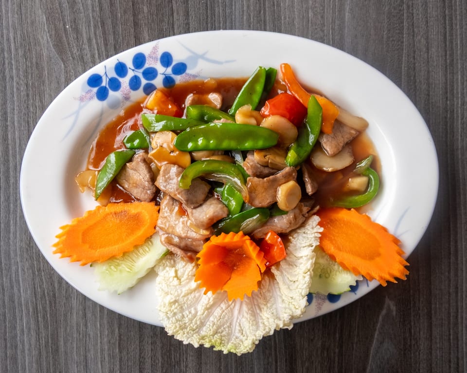 Slices of beef with green peppers, mushrooms, and carrots in a brown sauce on a white plate.