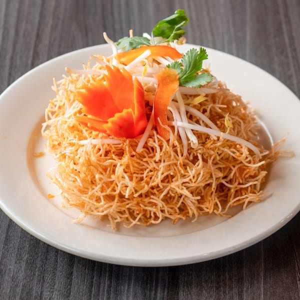 Crispy golden noodles topped with bean sprouts, cilantro, and carved carrot garnishes on a white plate.