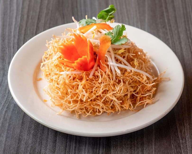 Crispy golden noodles topped with bean sprouts, cilantro, and carved carrot garnishes on a white plate.