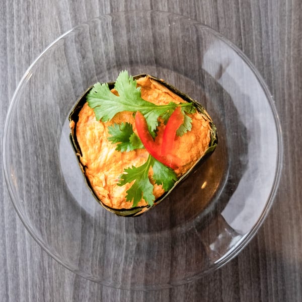Steamed curry custard, known as Hor Mok, garnished with cilantro and red chili on a clear plate.