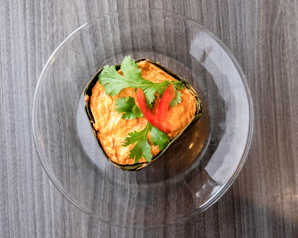 Steamed curry custard, known as Hor Mok, garnished with cilantro and red chili on a clear plate.
