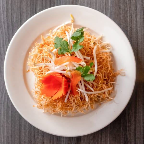 Crispy noodles with bean sprouts, cilantro, and carved carrots on a white plate.