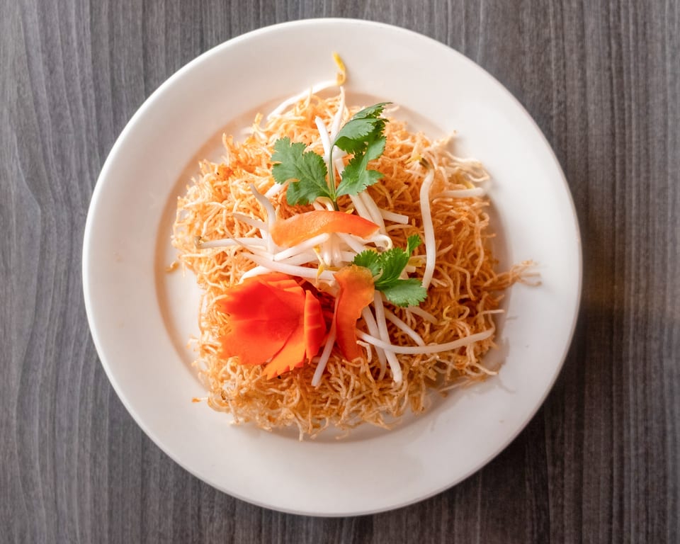 Crispy noodles with bean sprouts, cilantro, and carved carrots on a white plate.