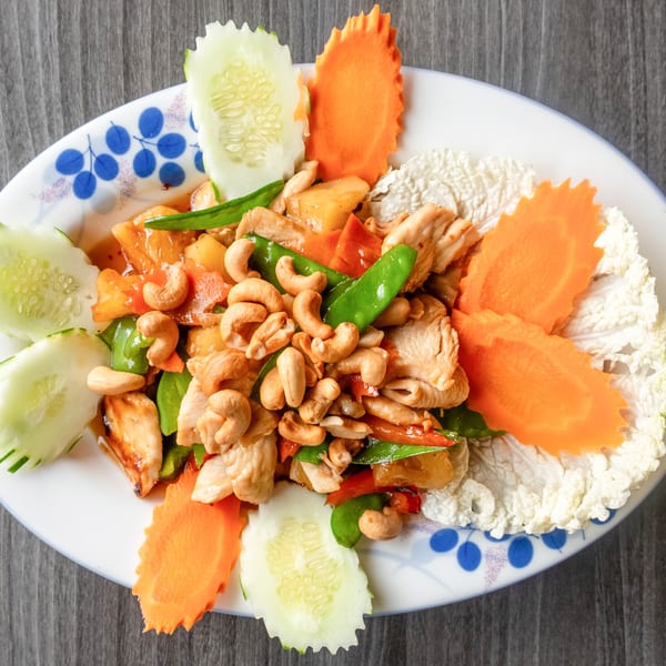 Cashew chicken stir-fry with pineapple, bell peppers, and snow peas, garnished with carved vegetables.
