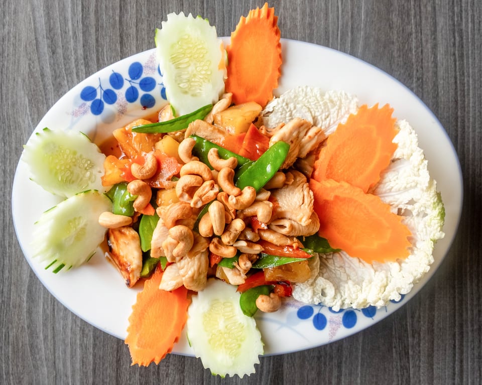 Cashew chicken stir-fry with pineapple, bell peppers, and snow peas, garnished with carved vegetables.